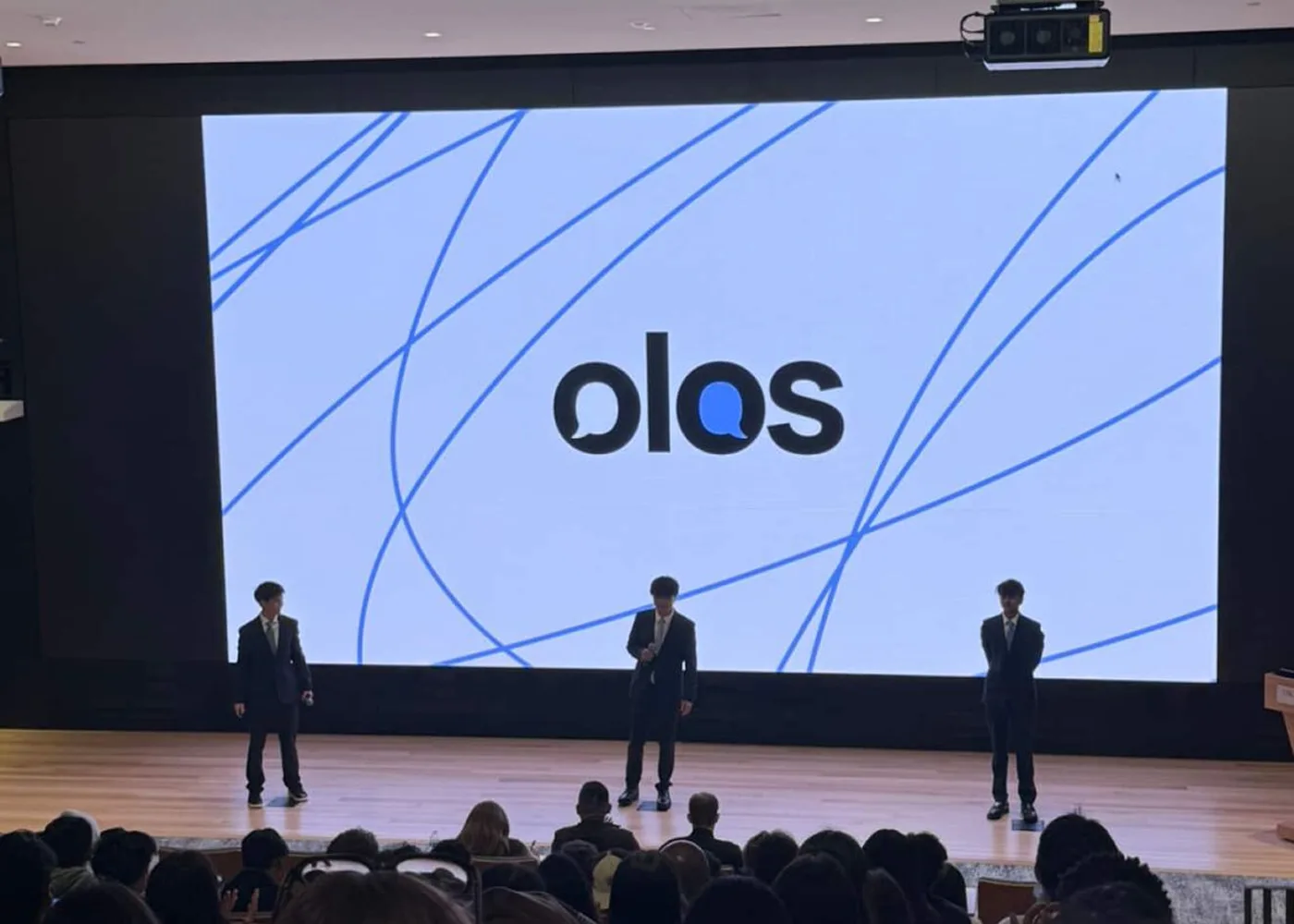 The Olos team on stage in front of the logo, at the end of a pitch.